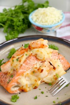 a piece of salmon covered in cheese and parsley on a plate with a fork