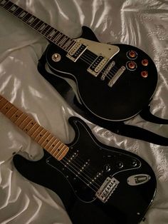 two electric guitars laying on top of a white sheet covered bed next to each other