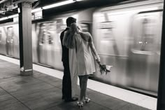 a man and woman standing next to each other in front of a train at a station