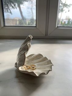 two gold wedding rings are placed on a shell shaped dish in front of a window