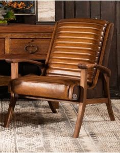 a brown leather chair sitting in front of a wooden desk with drawers and a painting on the wall