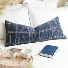 a bed with white pillows and a blue book on top of it next to a wicker tray