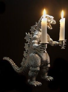 a godzilla holding a lit candle in it's hand