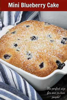 a blueberry cake in a white baking dish on top of a black and white striped towel