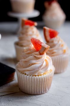 three cupcakes with white frosting and strawberries on top sitting on a table