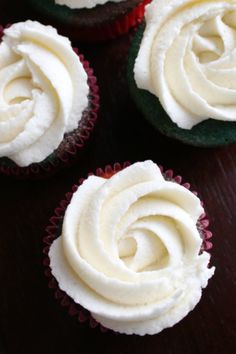 four cupcakes with white frosting sitting on a table