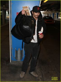 a man with a backpack and book in his hand is holding a drink while standing next to a blue wall