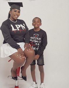 a woman sitting on top of a stool next to a little boy wearing a graduation cap