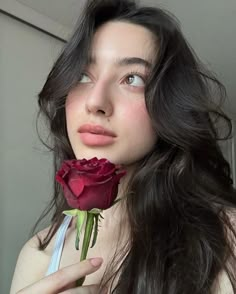 a woman with long hair holding a rose in her hand and looking at the camera