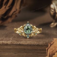 a ring with green and white stones sitting on top of a wooden table next to a book