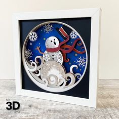 an ornament with a snowman on it in a white frame and blue background