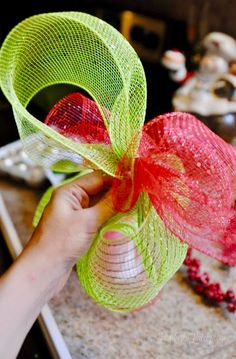 a hand holding a red and green mesh bow