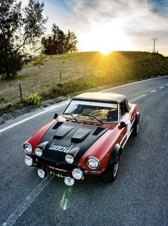 a red and black car driving down the road with the sun shining in the background