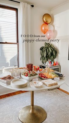 a white table topped with lots of food next to a large window filled with balloons