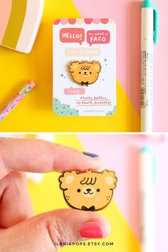 a hand holding a small bear shaped sticker on top of a yellow and pink background