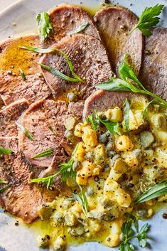 some meat and vegetables are on a white plate with green garnishes around it