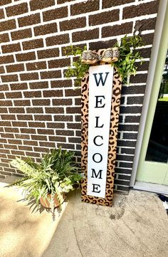 a welcome sign sitting on the side of a building next to a potted plant