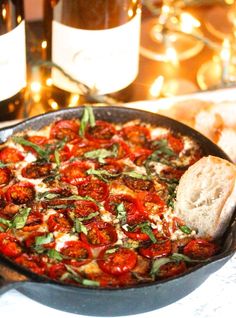 a pizza in a pan on a table with some wine bottles and candles behind it