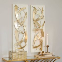 two metal art pieces sitting on top of a wooden shelf next to a candle holder