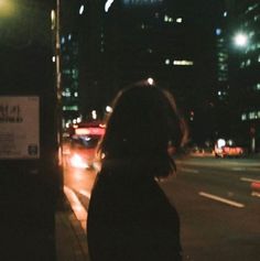 a woman standing next to a bus on a city street at night with buildings in the background