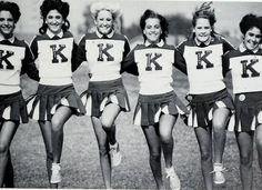 a group of young women standing next to each other on top of a grass covered field