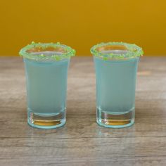 two shot glasses filled with blue liquid on top of a wooden table next to each other