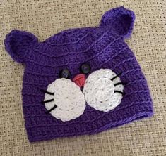 a purple knitted hat with eyes and ears on top of a brown tablecloth