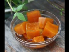 a glass bowl filled with cubed oranges on top of a wooden table next to a green plant