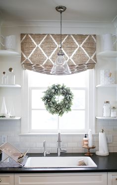 a kitchen sink under a window with a wreath hanging from it's valance