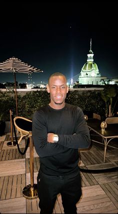 a man is standing on a deck with an umbrella in the background and his arms crossed