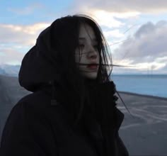 a woman with black hair and white make - up looks out over the ocean