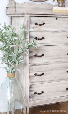 a white dresser with a mirror and potted plant in it next to a vase