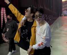 two young men standing next to each other in front of a stage holding wii controllers