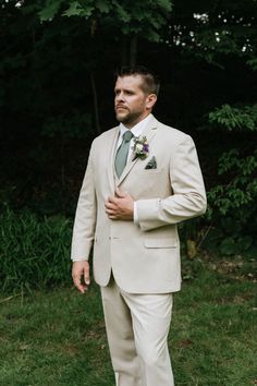 a man in a suit and tie standing on grass with trees in the back ground