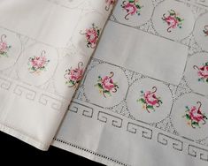 two pieces of white linen with pink flowers on them, one is folded up and the other has an embroidered border