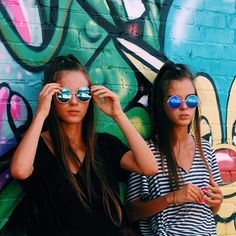 two young women are standing in front of a graffiti wall with sunglasses on their faces