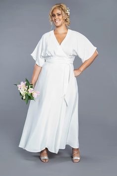 a woman wearing a white dress and holding a flower in her hand, standing against a gray background