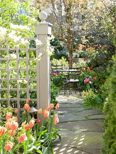 a garden with lots of flowers next to a table and chairs