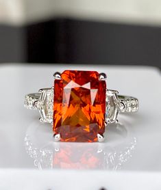 A Vivid Orange color Sapphire is a rare fine and breathtakingly gorgeous. Up For Sale is a Brand New 7.23 Carat plus (TCW) Certified 100% Natural Orange Sapphire Ring in Solid 18k White Gold, Size 6 (US).  Center Stone is a Beautiful 6.55 Carat Octagon Cut 100% Natural, Gentle Heat only Sapphire from Sri Lanka that have very good and best Clarity. The gemstone is Bright Orange Color and it certainly stands out. This stunning stone has a nicely shaped Octagon cut with really good symmetry and exc Luxury Orange Sterling Silver Jewelry, Orange Brilliant Cut Jewelry For Gift, Luxury Radiant Cut Red Ring, Orange Emerald Cut Jewelry For Anniversary, Elegant Orange Emerald Cut Jewelry, Orange Engagement Ring, Orange Ring, Saphir Ring, Red Sapphire