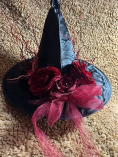 a black hat with red flowers on it sitting on the floor next to a pink ribbon