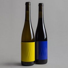 two bottles of wine sitting next to each other on a gray surface with yellow and blue labels