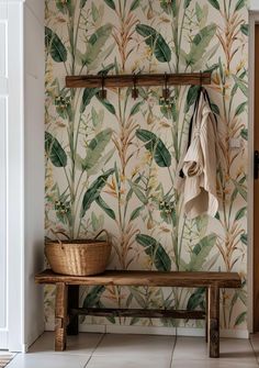 a wooden bench sitting next to a wall covered in green leafy wallpaper and a coat rack