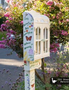 a mailbox with butterflies painted on it in front of some bushes and flowers outside