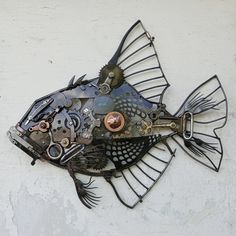 a metal fish sculpture on the side of a building with lots of gears attached to it