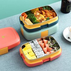 two bento boxes filled with food sitting on a table next to a cup of coffee