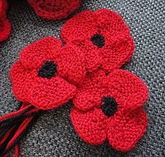 crocheted red flowers with black centers sitting on a gray surface next to yarn balls