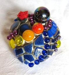 a colorful brooch sitting on top of a white cloth covered table next to a red rose