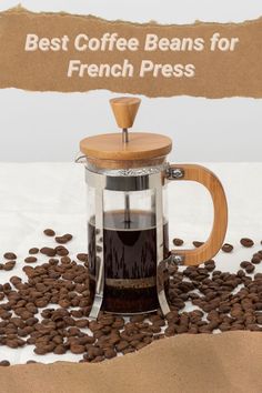 a french press coffee maker surrounded by coffee beans and paper sign that says best coffee beans for french press