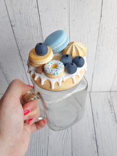 a person holding a glass cup filled with donuts and pastries on top of it