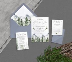 the wedding stationery is set up on top of a tree trunk, and features an evergreen - themed mountain scene